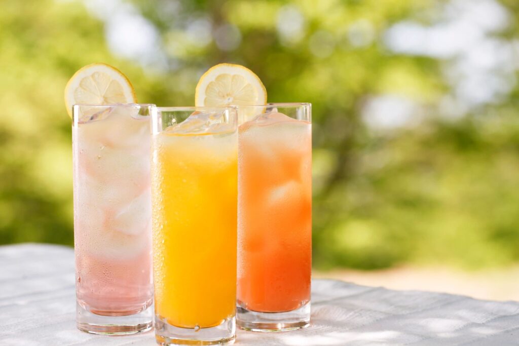 3 sparkling juices of different flavours sit on top of a table in the summer